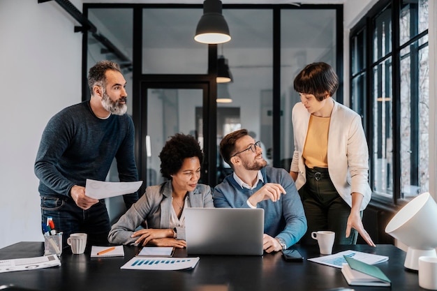 Een groep zakenmensen staat en zit op kantoor en werkt aan een project op een laptop