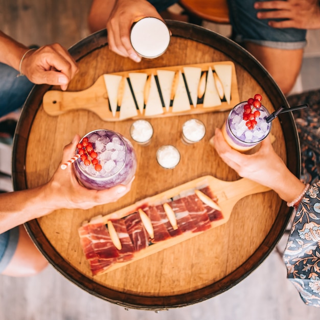 Een groepje vrienden zit 's zomers op het terras achter een houten vat met cocktails en een hapje