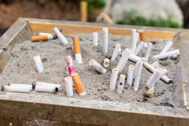 Een groot aantal sigarettenpeuken met een filter, gedoofd in een urn op straat in het zand. vre roken, kkantsergens en kanker