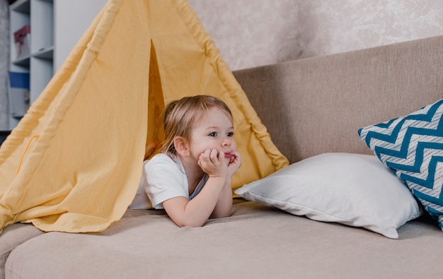 Een groot portret van een klein meisje dat in een gele tipi ligt. het droevige gezicht van een kind