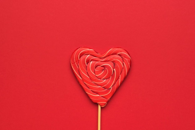 Een groot rood snoepje op een stokje in de vorm van een hart op een rode achtergrond Minimaal concept van zoet leven en liefde