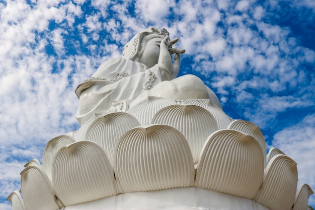 Een groot wit Guan Yin-beeld op de helling achter de hemel en zonlicht overdag.