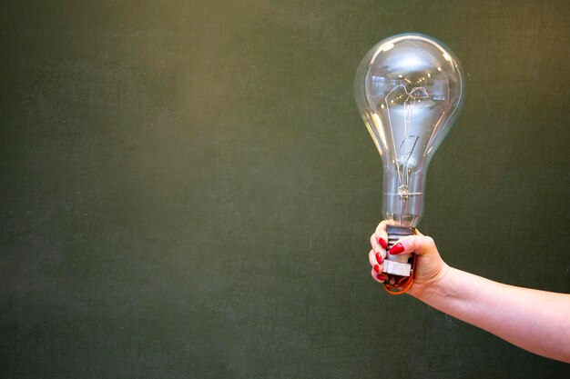 Een grote gloeilamp in de hand van het meisje tegen de achtergrond van het schoolbord