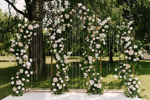 Een grote gouden boog met een wit podium versierd met bloemen in de natuur