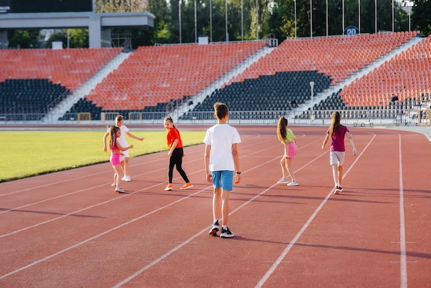 Een grote groep kinderen, jongens en meisjes, rennen en sporten in het stadion tijdens zonsondergang. Een gezonde leefstijl.