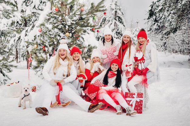 Een grote groep meisjes met kerstcadeaus in hun handen die in het winterbos staan. Meisjes in rode en witte kleding met kerstcadeaus in het besneeuwde bos