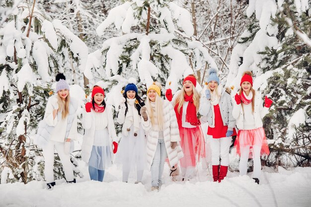 Een grote groep meisjes met lolly's in hun handen staat in het winterbos. Meisjes in rode en witte kleren met snoep in een besneeuwd bos.