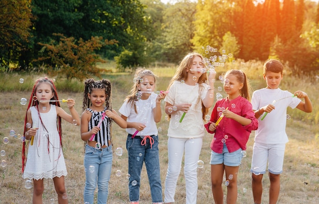 Een grote groep vrolijke kinderen speelt in het Park en blaast zeepbellen op