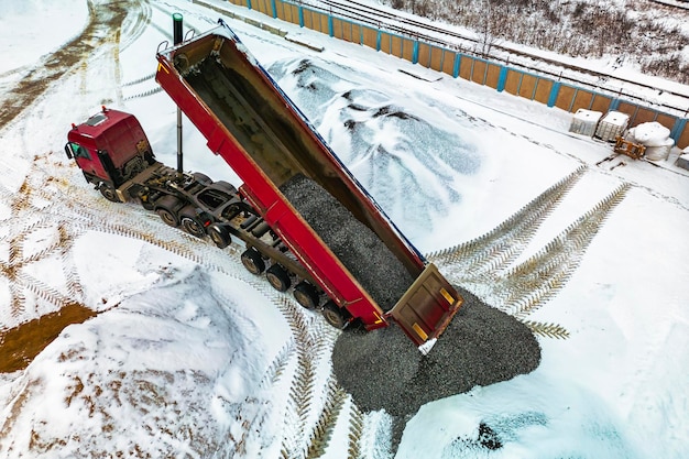 Een grote kiepwagen lost puin of grind op een bouwplaats in de winter Autotonar voor het vervoeren van zware bulklading Bouwplaats voorzien van materialen Bouwen in de sneeuw