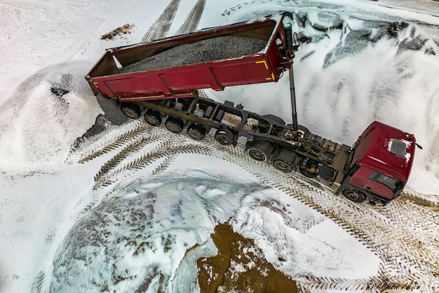 Een grote kiepwagen lost puin of grind op een bouwplaats in de winter Autotonar voor het vervoeren van zware bulklading Bouwplaats voorzien van materialen Bouwen in de sneeuw