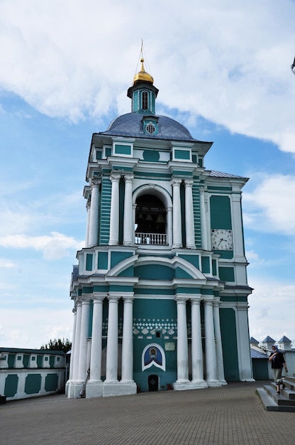 Een grote klokkentoren met een belfort en een klok. De vrouw draagt een gaasmasker. 01 augustus 2021, Bryansk, Rusland.