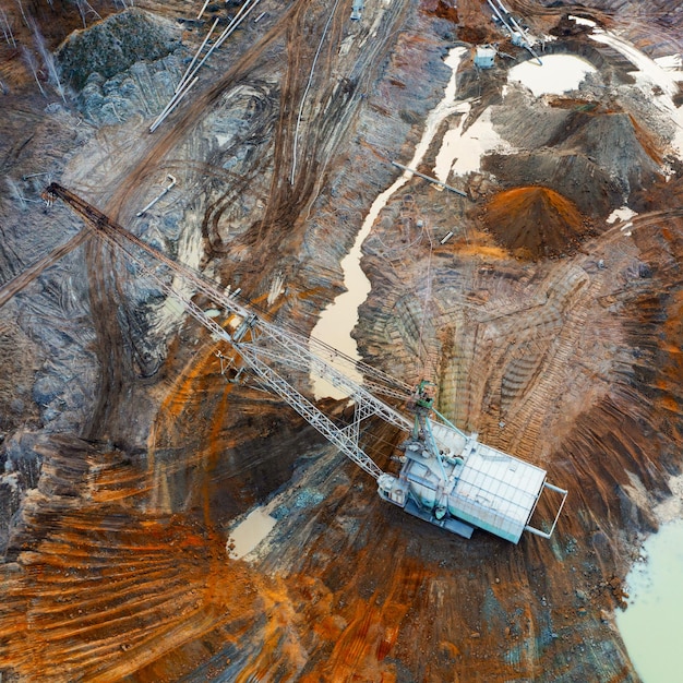 Een grote lopende graafmachine werkt in een steengroeve voor de winning van zeldzame metalen. Drone-weergave. Industrieel landschap.