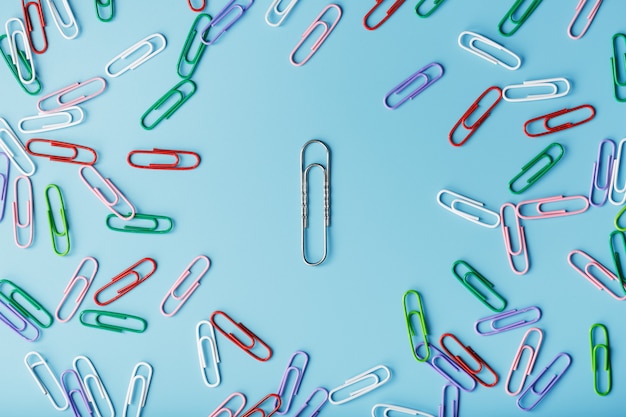 Een grote paperclip omgeven door kleine gekleurde paperclips op een blauwe achtergrond