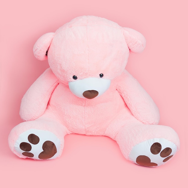 Een grote roze teddybeer zit op een roze achtergrond