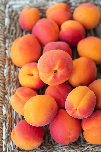 Een grote stapel rijpe feloranje abrikozen ligt dicht op een rieten bord