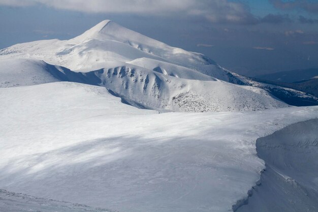 Een grote witte rotsachtige berg met een donkere couloir is bedekt met sneeuw tussen de mistige wolken voor de winterstorm