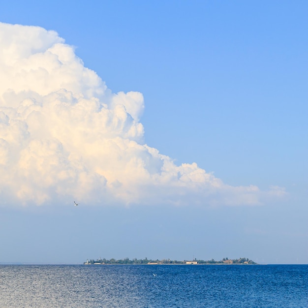 Een grote witte wolk boven de zee een zeemeeuw in de lucht en een eiland