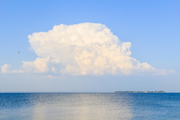 Een grote witte wolk boven de zee een zeemeeuw in de lucht en een eiland