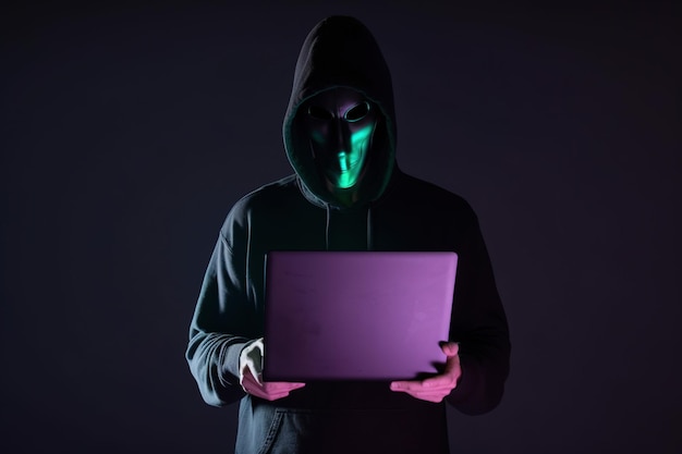 een hacker in een hoodie met behulp van een laptopcomputer geïsoleerd op een donkere achtergrond met neonlicht