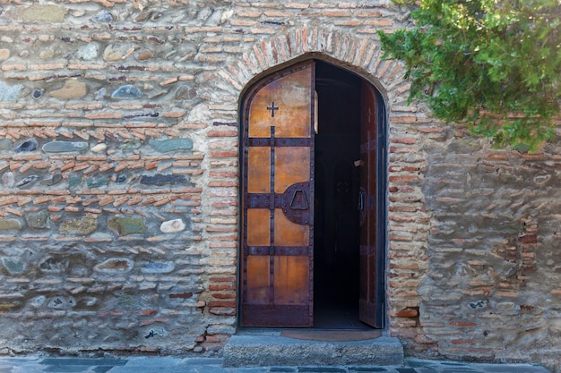 Een half open houten deur van de kerk tegen de achtergrond van een stenen muur. Houten deuren van de kerk.