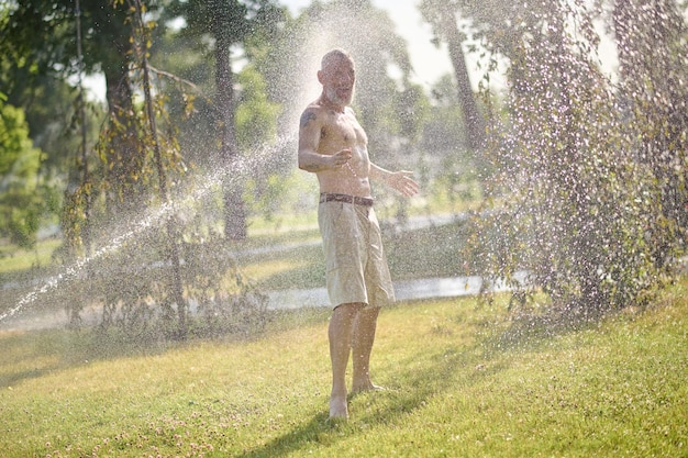 Een halfnaakte man in korte broek staat onder de douche in het park