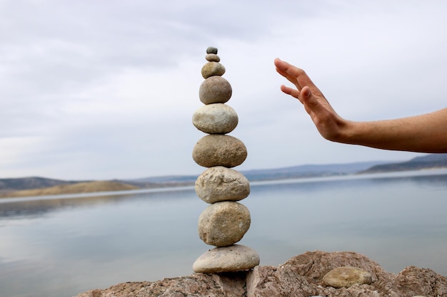 Een hand construeert evenwicht op kiezelstenen. Perfecte balans van stapel kiezelstenen aan de kust.