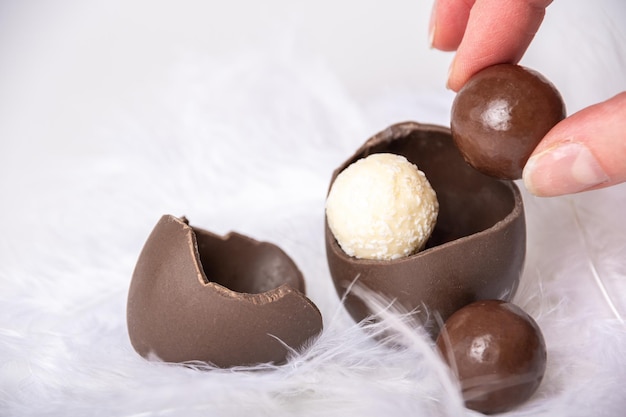Een hand die chocolade rond snoepjes neemt van een gebarsten chocolade-ei in een wit zacht verennest Zoete paastraditie Lentevakantie Paastraktatie voor kinderen