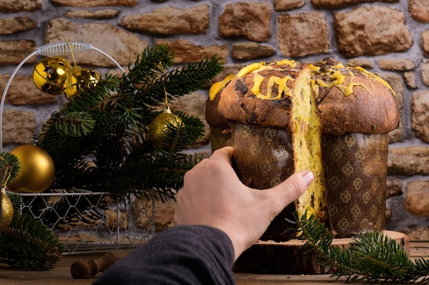 Een hand die een gesneden stuk traditionele italiaanse kerstcake-panettone neemt met feestelijke decoratie aan