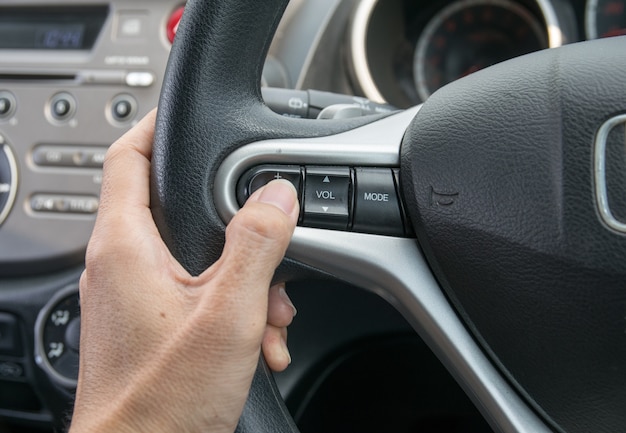 Een hand duwt de cruise control-knop op een stuur.