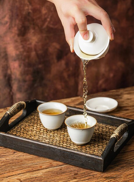 Een hand giet een kopje koffie uit een theepot in drie kopjes.