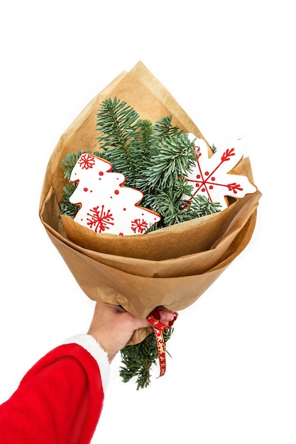 Een hand houdt een boeket takken van een kerstboom en twee peperkoekkoekjes vast. Geïsoleerd