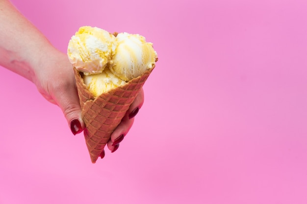 Een hand houdt een ijsje op een roze ijslollyachtergrond in een wafelkop.