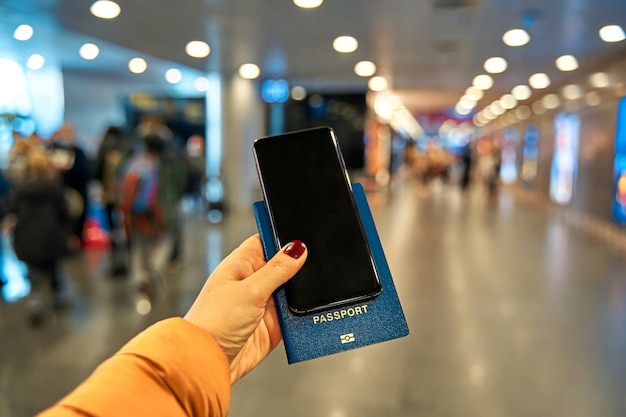 Foto een hand houdt een smartphone en een paspoort vast voor reizen op de luchthaven