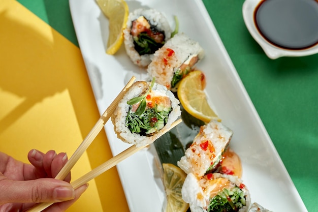 Een hand houdt een sushirol met roomkaas, komkommer en zalm vast op een lichte achtergrond.