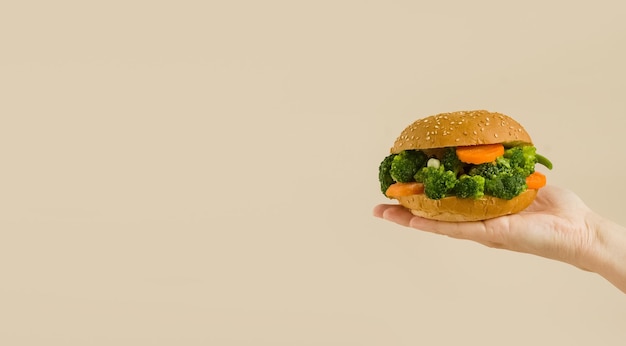 Foto een hand houdt een veganistische burger vast op een beige achtergrond veganistische burger met groenten, broccoli, wortelen, erwten