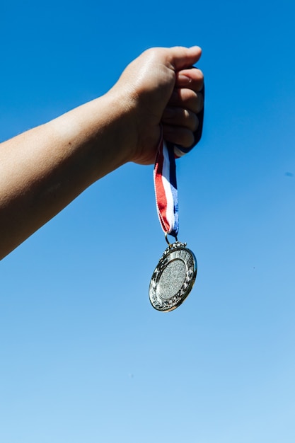 Een hand houdt een zilveren medaille op de tweede plaats omhoog, met de lucht op de achtergrond. Overwinning concept