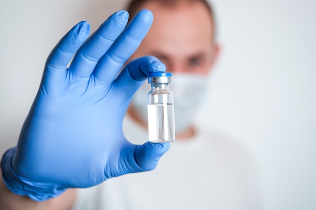 Een hand in blauwe beschermende handschoen met een ampul met een medicijn en een wazige man op de achtergrond