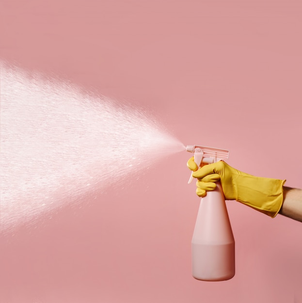 Een hand in een huishoudhandschoen van siliconen houdt een fles met vloeibare spray vast.