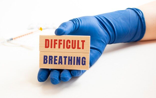 Een hand in een medische handschoen houdt houten kubussen vast met de inscriptie "moeilijke ademhaling"