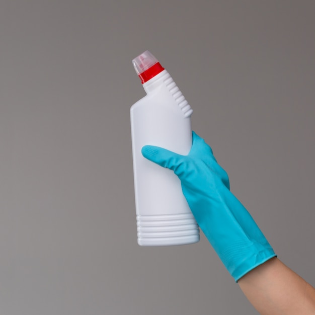 Een hand in een rubberhandschoen houdt een fles loodgietend detergens o