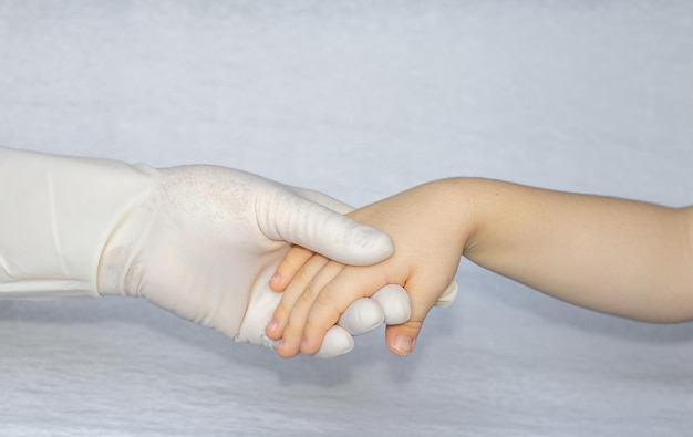 Een hand in een witte handschoen houdt een kinderhand vast zonder handschoen medisch concept zelfzorgondersteuning van