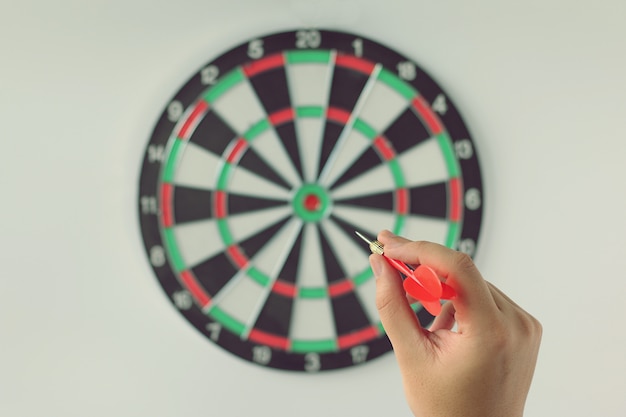 Een hand met een dart klaar om te richten op het dartboard op witte muur