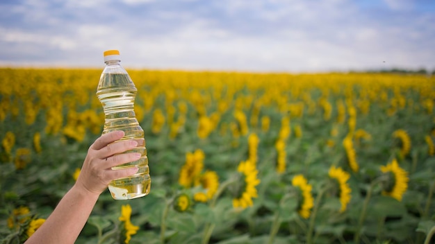 Een hand met een fles gouden zonnebloemolie opgewekt tegen de achtergrond van een veld met bloeiende zonnebloemen in een zonnige kopieerruimte