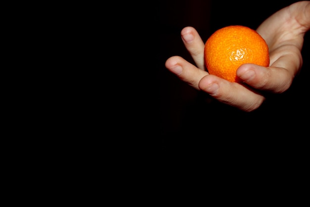 een hand met een oranje mandarijn op een zwarte achtergrond