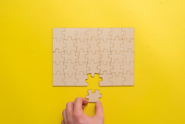 Foto een hand met een puzzelstukje en een complete puzzel op tafel