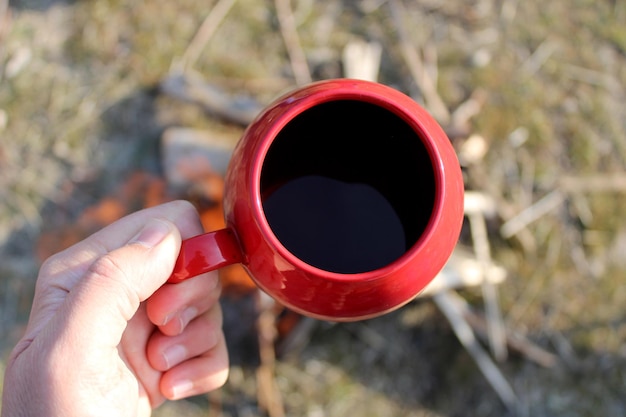 Een hand met een rode mok met koffie erin.