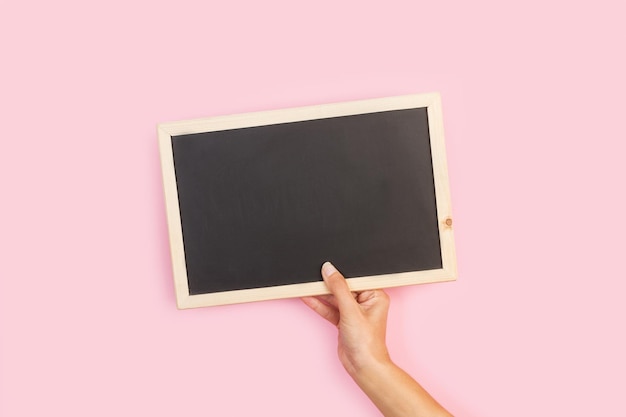 Een hand met een schoolbord met een houten frame op een roze achtergrond.
