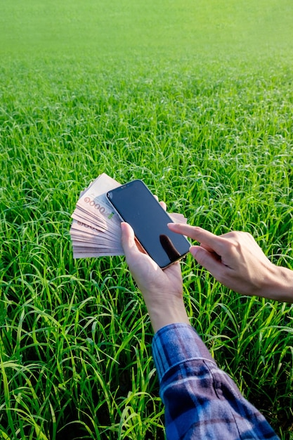 Een hand met een smartphone op het gras in een park met geld biljet omringd door natuur en technologie