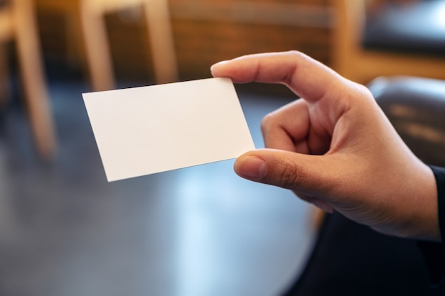 Een hand met een wit leeg visitekaartje met onscherpe achtergrond