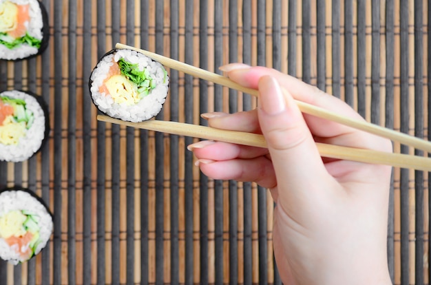 Een hand met eetstokjes houdt een sushi-roll op een bamboe stro serwing mat achtergrond